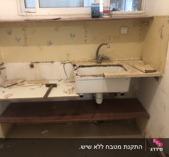 מטבח ישן עם כיור, מדפים וקיר מתקלף